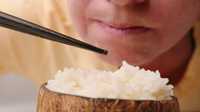Man eats boiled rice from bowl with chopsticks close-up.