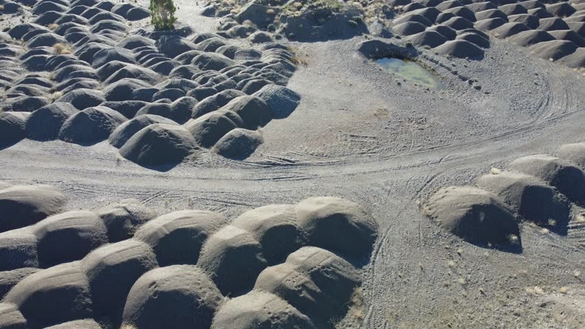 desert landscape filmed from a drone. hundreds of small mounds of aggregate, all identical, among which you can see a solitary tree