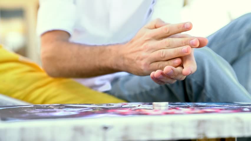 Young man in white shirt is playing board game, he rolls die to make move of chips, hands close-up.