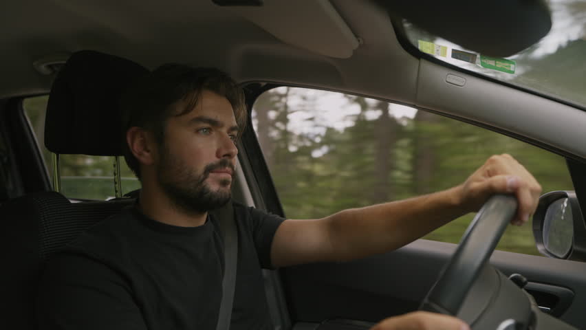 Young caucasian man driving and looking around. Profile medium shot