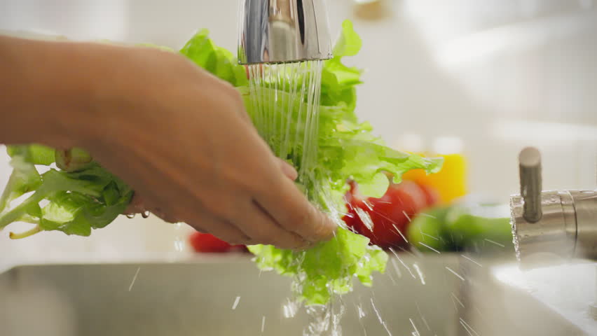 Food. Young man in home clothes concentratedly cleans fresh lettuce in home kitchen. Female athlete washes lettuce under water current approaches to cooking healthy food, splashes