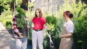 A loving multiracial couple, dressed in red, selects a tree for their home at a garden center, while a female staff member provides them with expert advice and assistance - Powered by Shutterstock - Get 15% off with code: PIKWIZARD15