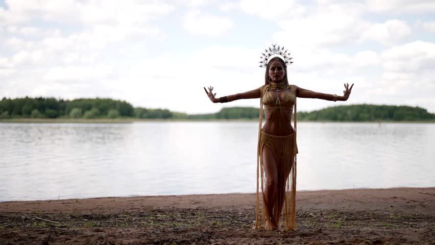 A woman in a crown and an exotic costume gracefully dances by the lake, the blue sky with clouds emphasizes her grace and lightness.