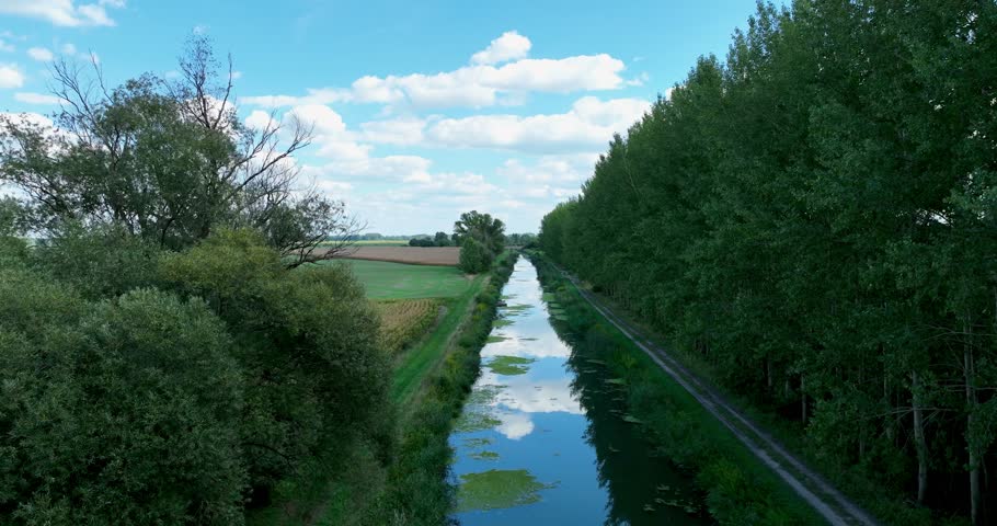 Aerial view of water canal during summer with clouds and blue sky. Flying above water and agricultural land