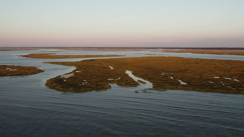 Marsh swamp land of barrier islands connect to open ocean at sunset, aerial dolly