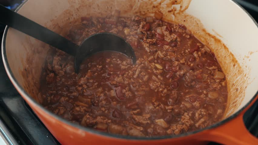 Scooping homemade chili in an orange bowl 