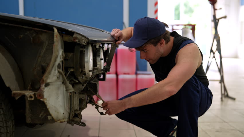 Auto mechanic repairman examining front of car without bumper, assessing plan for future work in automobile repair and renew service station. Concept of car service, repair and maintenance.