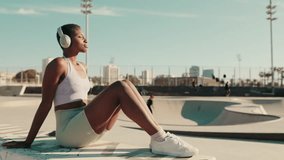 A young athletic woman sits in a skatepark on a hot summer day, with skateboarders performing tricks in the background - Powered by Shutterstock - Get 15% off with code: PIKWIZARD15