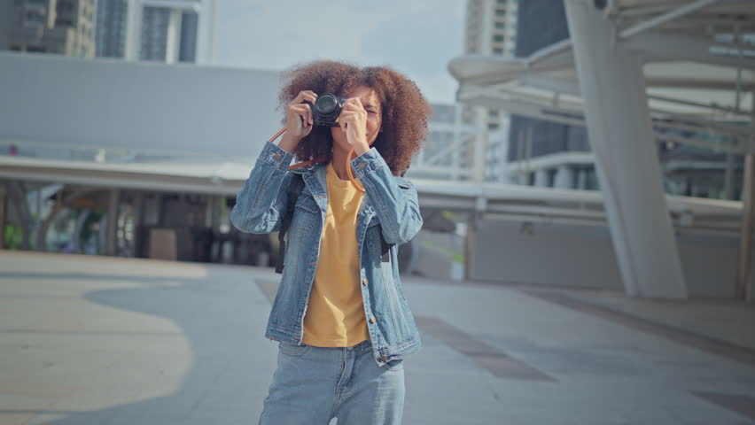 Happy young tourist Mixed race woman in good mood with camera standing outdoors in city, Smile young female tourist taking photo. Photographer taking pictures. Enjoying travel concept