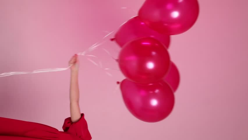 A young girl is holding four red balloons in her hand. She is sitting on the ground and looking up at the balloons. Concept of innocence and joy, as the girl is surrounded by the colorful balloons