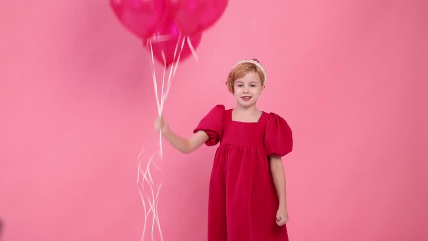 A young girl is holding four red balloons in her hand. She is sitting on the ground and looking up at the balloons. Concept of innocence and joy, as the girl is surrounded by the colorful balloons