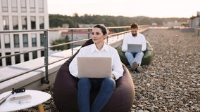 Business professionals working on laptops while seated on bean bags on office rooftop. Relaxed work environment embracing outdoor, flexible workspace concept. - Powered by Shutterstock - Get 15% off with code: PIKWIZARD15
