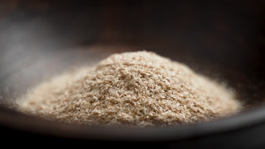 Medicinal isabgol or psyllium husks falling in slow motion into a brown wooden bowl close up