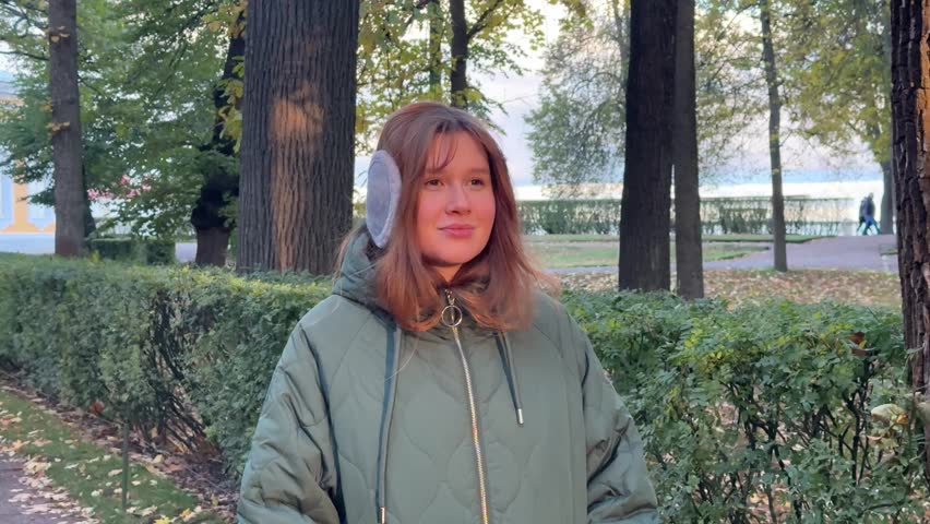 Beautiful young woman in ear muffs walking in the park in autumn. Enjoying the weather, smiling, breathing fresh air