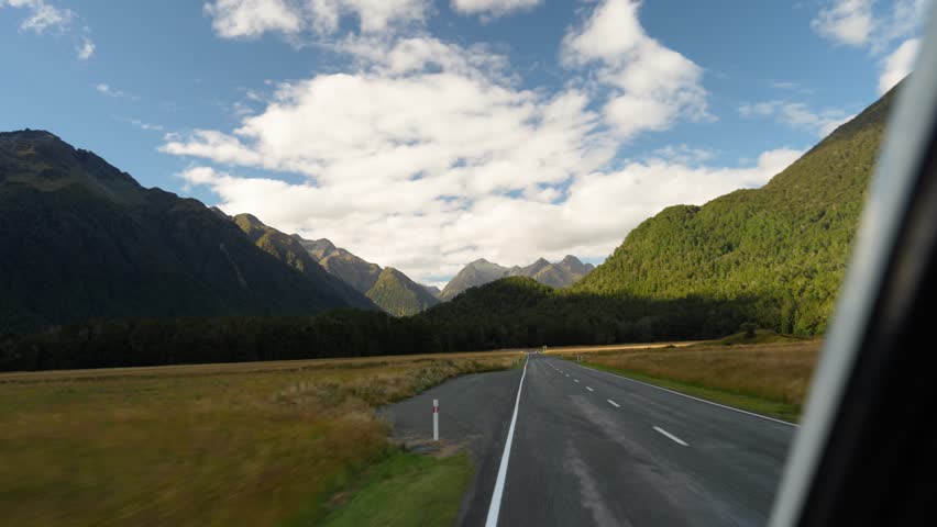 Scenic road in New Zealand leading towards a mountain range, with a clear sky and lush green landscape