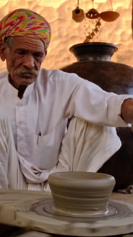 Skilled professional potter throwing the potter's wheel and shaping traditional ceramic vessel and clay ware: pot, jar in pottery workshop. Handwork craft from Shilpagram, Udaipur, Rajasthan, India