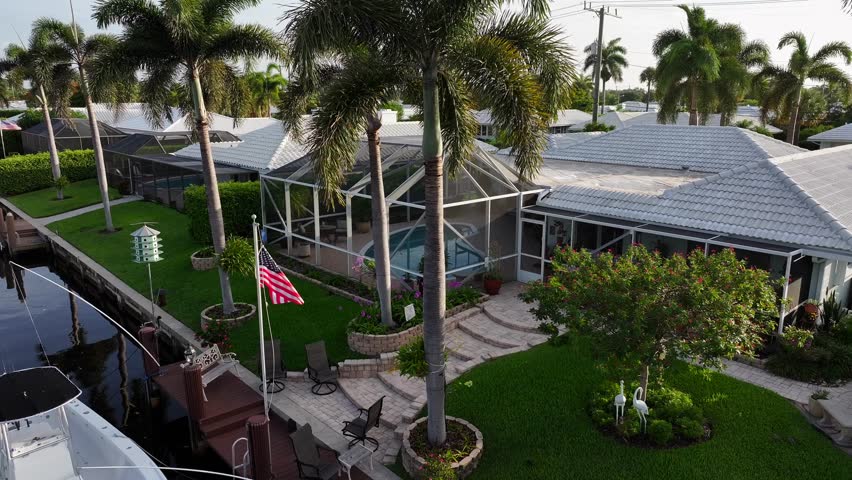 Patriotic american flag in garden of luxury mansion with swimming pool. Palm trees and large villas in suburb of Boca Raton, USA. River with private access. Rising drone wide shot.