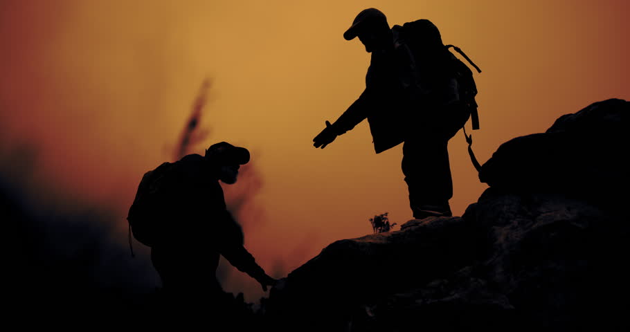 Sunset, mountain and silhouette of men helping on cliff for view in nature with camping backpack and support. Outdoor, travel and adventure with journey, trekking and trip at dusk with friends hiking