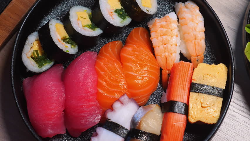 Assorted sushi platter with various types of nigiri, maki rolls, and sashimi on black plate, showcasing Japanese cuisine. Authentic Japanese Food and Culinary Arts.