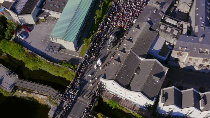 Aerial top-down view of the Galway International Arts Festival parade with crowds following as it approaches the River Corrib.