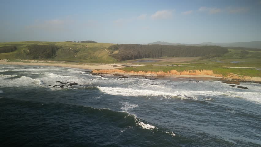 Aerial drone footage over Pescadero State Beach from the Peninsula of Northern California. The coastline features rugged cliffs, sandy shores, and crashing waves, all bathed in golden sunlight.
