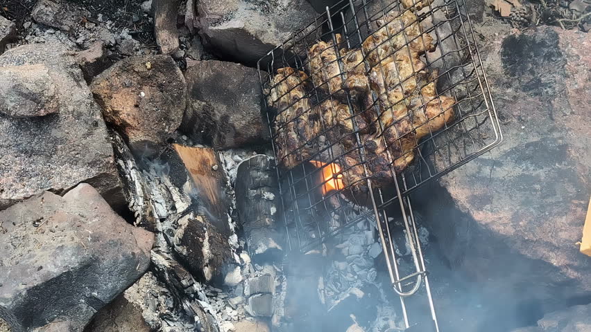 Meat on a grill to bbq on the beach in the sand, fireplace with rocks around, closeup in slow motion, static shot
