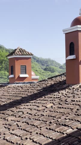 View of a terra cotta tile rooftop in Costa Rica with rainforest in the background and blue sky.