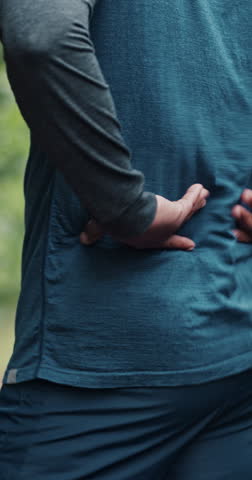 Outdoor, back pain and person with fitness, injury and tired with fatigue, burnout and training. Stretching, massage and runner with inflammation, nature and muscle strain with problem or risk