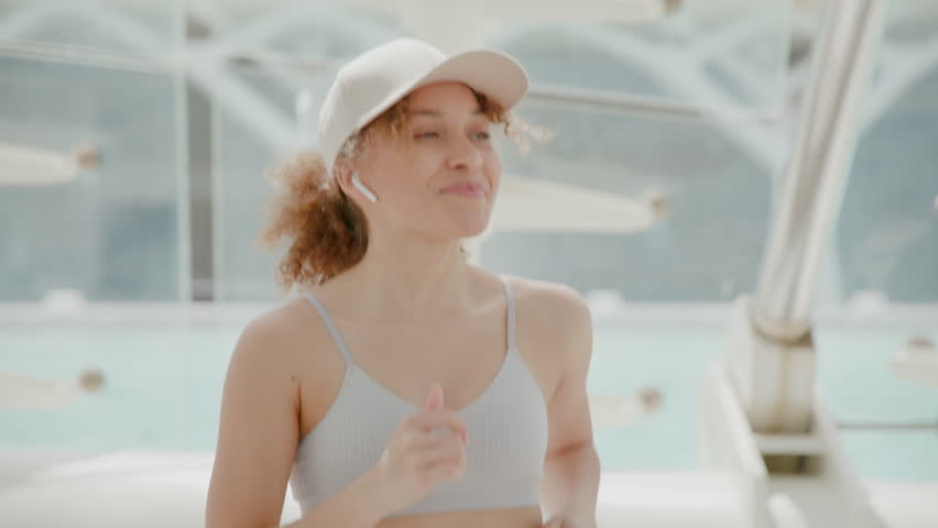 In the bright sunlit scene, a young woman in activewear is jogging and smiling on a boat. She represents an attractive, joyful, and active lifestyle, embodying themes of adventure and happiness