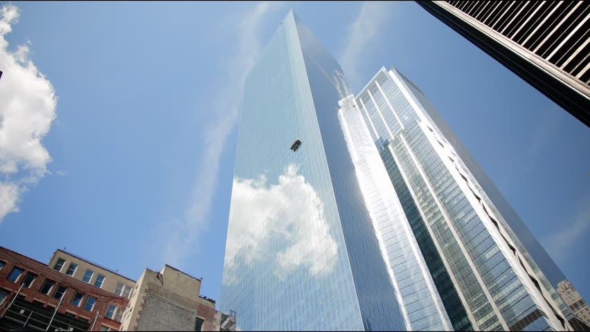 In the video frames, modern glass skyscrapers in New York City are reflected against a clear blue sky with clouds, showcasing the citys elegant architecture and futuristic skyline