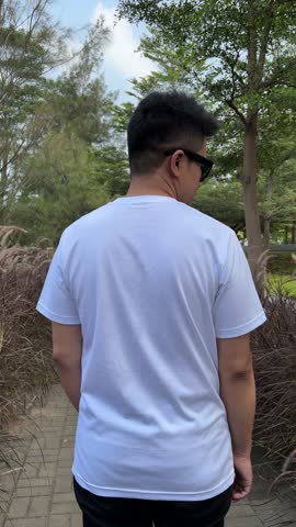 Rear view of a man posing wearing a white short sleeved T-shirt and sunglasses outdoors