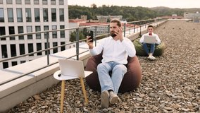 Two remote workers on rooftop using laptops and smartphones. Bean bag seating and casual work environment outdoors over city skyline - Powered by Shutterstock - Get 15% off with code: PIKWIZARD15