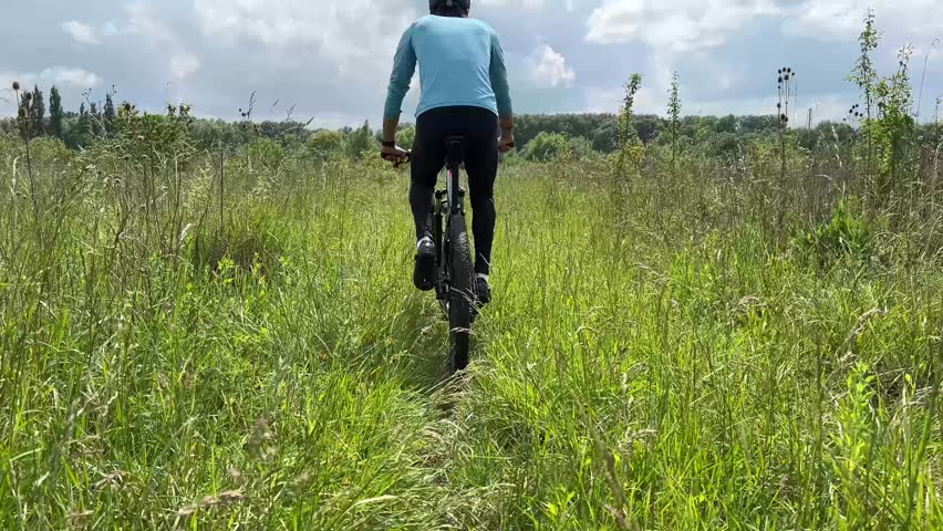 Cyclist exploring a lush, sunny meadow, surrounded by tall grass and vibrant scenery. Enjoy outdoor adventure and nature at its best