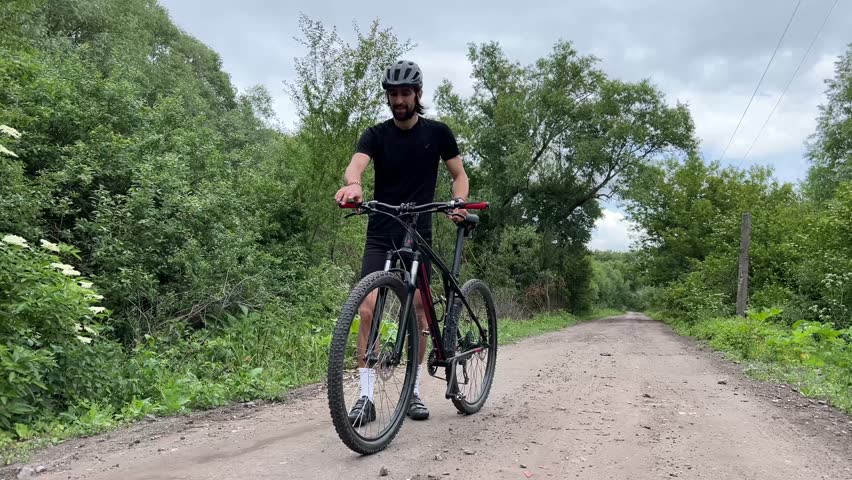 Man cycling on tranquil rural dirt road surrounded by lush greenery and trees under a cloudy sky