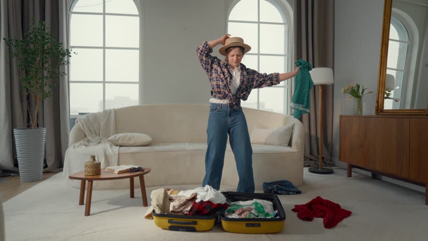 Dream about summer vacation, woman packing suitcase in living room, portrait. Female tourist choosing clothes for walk on seashore in south country, carefree joyful lady putting things in travel bag