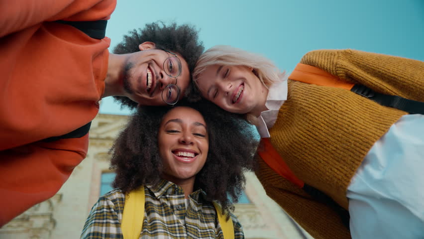 Bottom view three friends buddies students leaning heads African women girls females Caucasian man guy male looking at camera smiling city outdoors university college high school education friendship