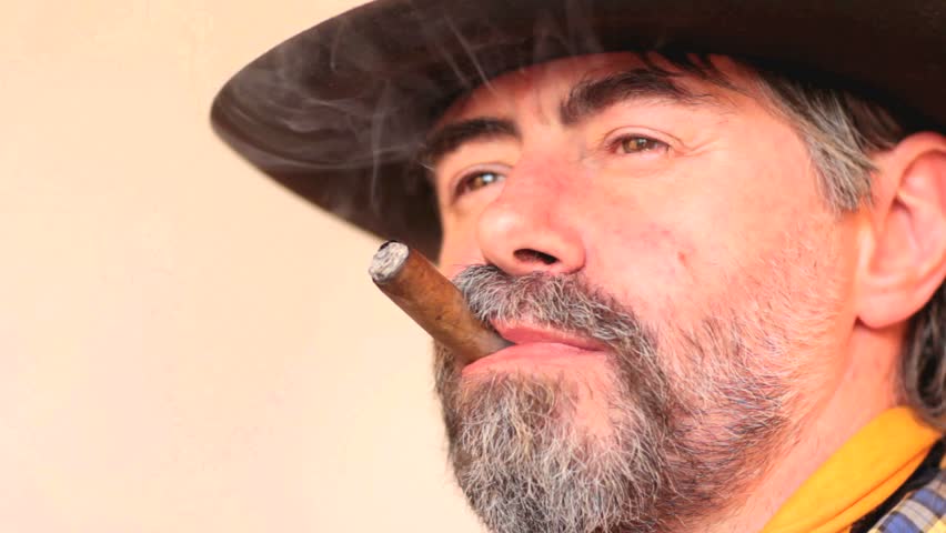 Closeup portrait of cowboy looking at copy space, smoking cigar and laughing. on