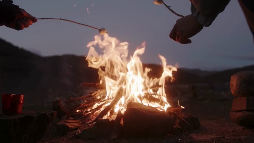 Cooking a marshmellow on stick close to a barbecue grill fireplace in a forest. Close up, panning, and sliding shot, real time, no people. Shallow depth of field. late evening