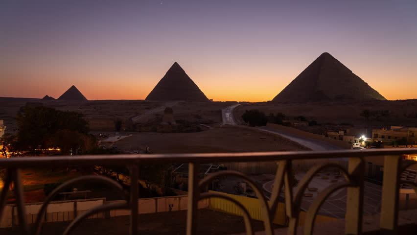 Day to night timelapse with the light show of the 3 famous pyramids in Giza near Cairo. Taken through a fence at a nearby hotel