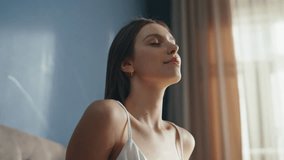 Tranquil woman stretching in bed early morning closeup. Smiling girl waking up in cozy sunlit bedroom feeling rejuvenated. Happy awakening lady enjoying lazy weekend at home. Brunette in white pajamas - Powered by Shutterstock - Get 15% off with code: PIKWIZARD15