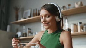 Headphones girl eating breakfast in modern kitchen listening to music closeup. Smiling woman enjoying healthy porridge in contemporary kitchen. Happy lady having cereal with milk in cozy cuisine. - Powered by Shutterstock - Get 15% off with code: PIKWIZARD15