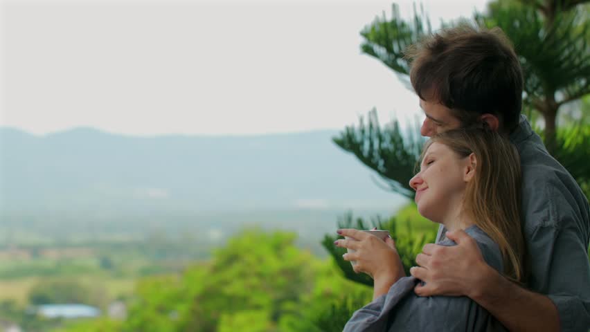 Young couple enjoying peaceful morning embrace while watching calm and serene nature view on balcony.