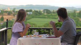 Young couple having breakfast at outdoor dining area with scenic countryside view in background. Appear engaged in relaxed conversation while enjoying natural surroundings and fresh air. - Powered by Shutterstock - Get 15% off with code: PIKWIZARD15