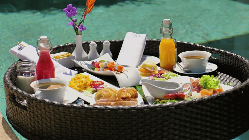 Luxurious floating breakfast tray in swimming pool at tropical resort. Gourmet holiday experience with fresh fruits, pastries, juices, and hot beverages. Exotic vacation dining and leisure.