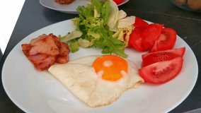 A balanced breakfast plate featuring a perfectly fried sunny-side-up egg, crispy bacon, fresh green salad leaves, and sliced ripe tomatoes, arranged on a white dish. ideal for promoting healthy eating - Powered by Shutterstock - Get 15% off with code: PIKWIZARD15