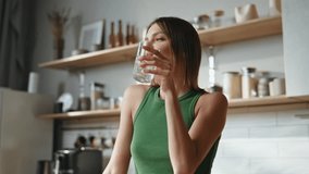 Morning girl taking water glass at modern kitchen enjoying domestic weekend closeup. Smiling woman drinking liquid starting day at home. Relaxed lady stretching hands refreshing with cold beverage. - Powered by Shutterstock - Get 15% off with code: PIKWIZARD15
