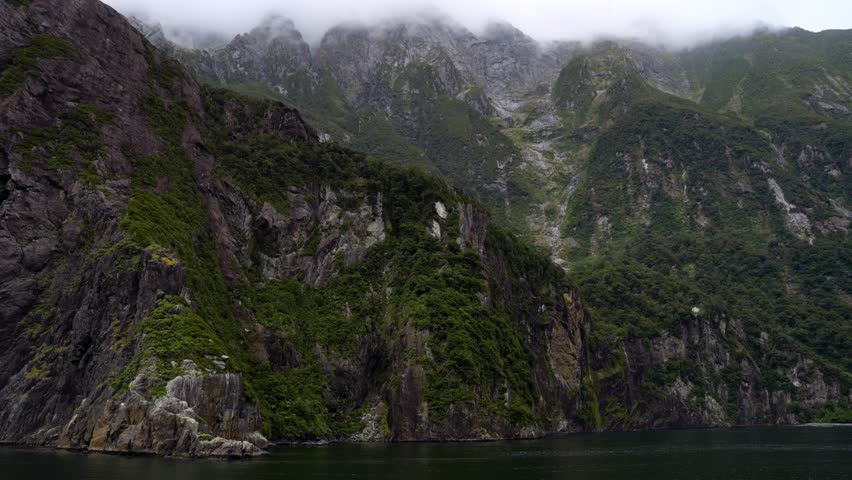 View of the sheer rugged mountains of the Milford Sound with peaks hidden in the clouds