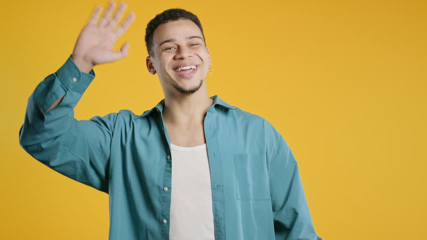 Friendly young African American man waving hand - hello, or goodbye, chao, salute. Parting, say bye to camera. Handsome man on yellow studio background. High quality 4k footage