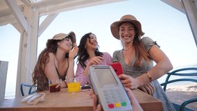 Happy young group of only women paying the bill with a nfc cellphone in cocktail beach bar. Female holding a smart phone and giving a payment transaction to the cashier on vacations with her friends - Powered by Shutterstock - Get 15% off with code: PIKWIZARD15