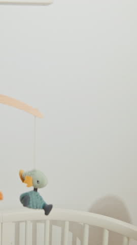 Silhouettes on white wall of the mother that playing with her little baby. Shadows near white cot with colourful crib mobile.